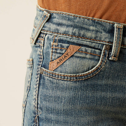 Boy's Ariat B5 slim straight jean in a medium wash. Close up of pocket showing Ariat logo tag.