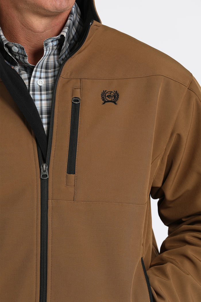 Brown Cinch bonded jacket. Closeup view of Cinch embroidered black logo and phone pocket zipper of left chest.