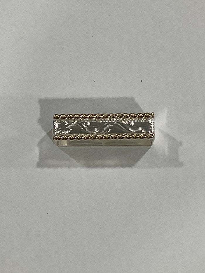 A small rectangular silver-toned metal charm with an engraved floral pattern and a textured gold-toned beaded border, shown on a plain light gray background.