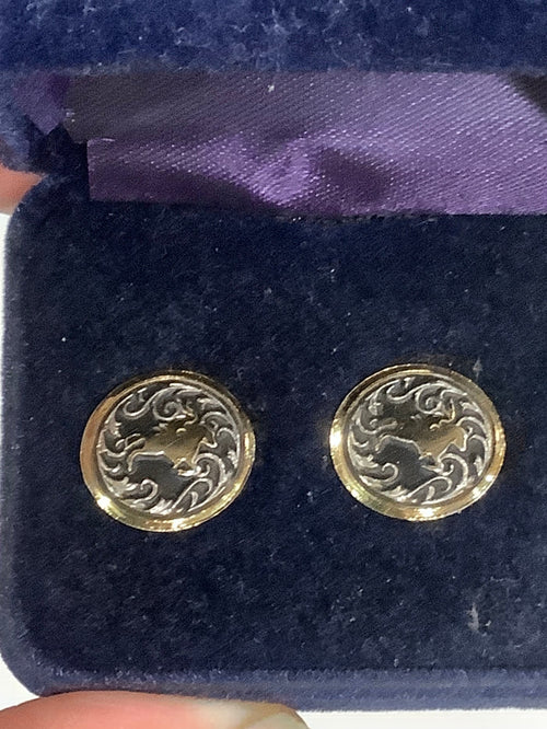 A pair of round gold-toned stud earrings with an engraved floral or scroll pattern, displayed on a dark blue velvet jewelry box.