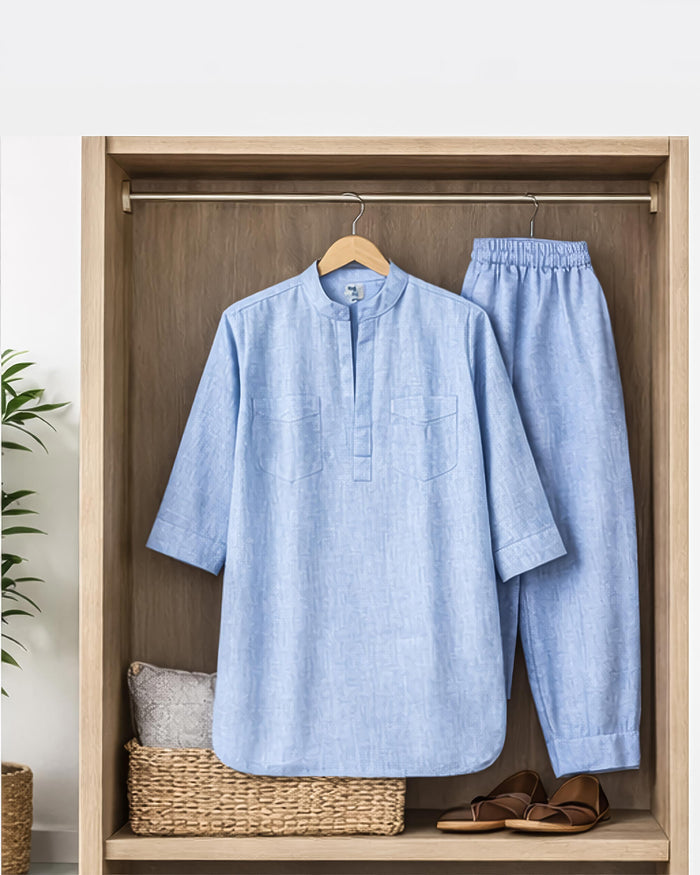 Light blue shirt and pants hanging on a wooden wardrobe with a plant and basket in the background.